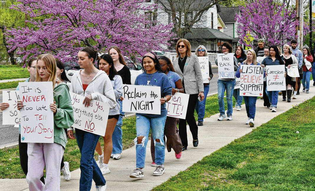 A crowd walks down a sidewalk with signs encouraging support and reclaiming identity